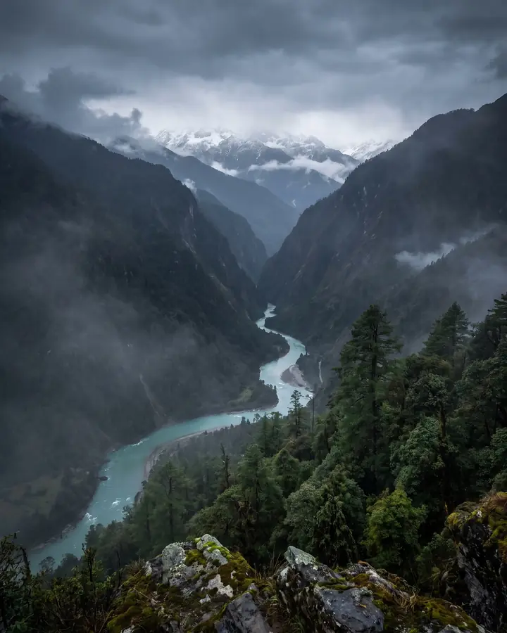 A river flowing out of a dark mountain gorge into forested hills.