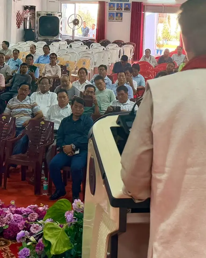 Photo of a speaker addressing a large seated audience at a public meeting in a hall.