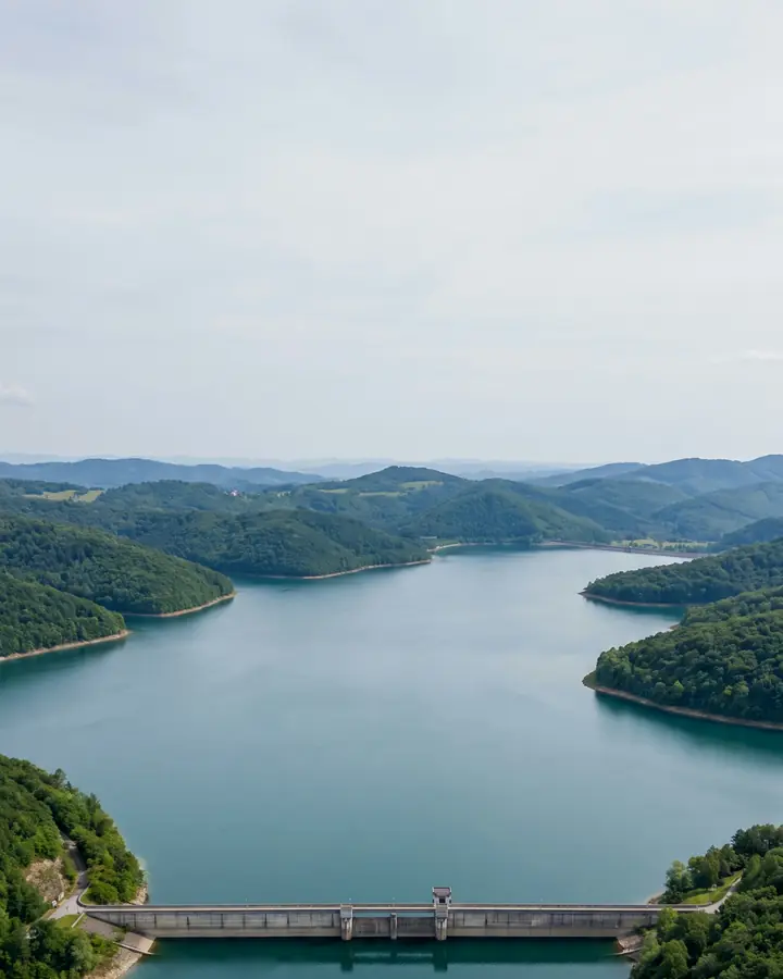 Aerial image of an ordinary, unnamed dam holding a reservoir in green hills, with two drawn bars to scale labelled Medog, China, about 5.5 and SUMP, about 9.2 billion cubic metres.